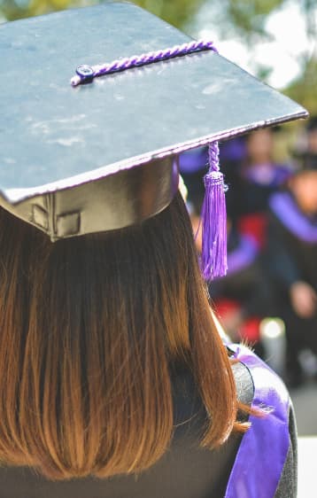 Shot of the back of a woman's head, wearing a graduation cap and gown.