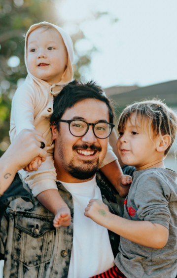 Man holding a kid with a baby on his shoulders