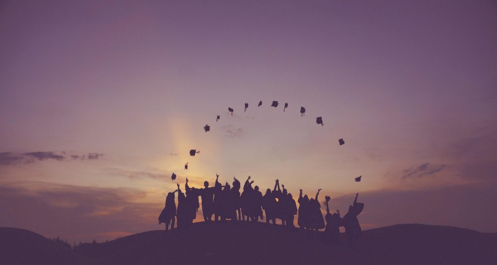 Graduates throwing caps in the air at sunset