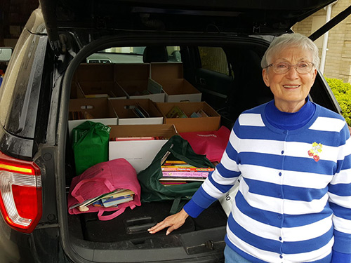 A woman stands by the open trunk of her car, which is full of helpful items for incarcerated women.