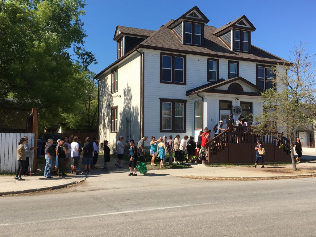 Lineup of people outside of a stately, white historical home on a sunny day with a bright blue sky.