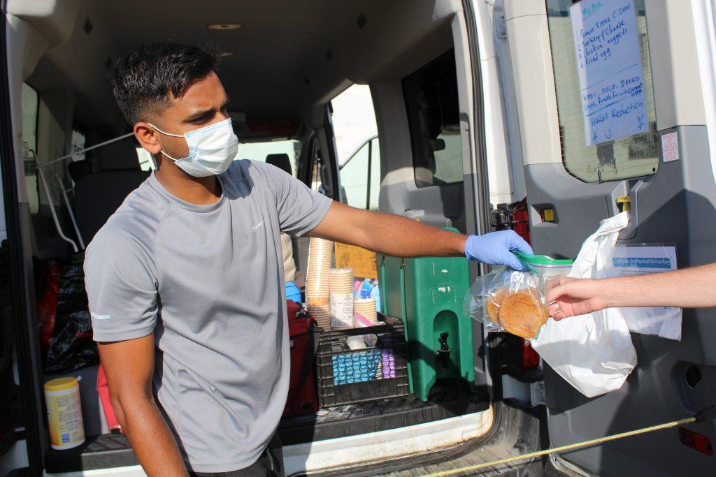 Masked volunteer giving food out from the back of a van.