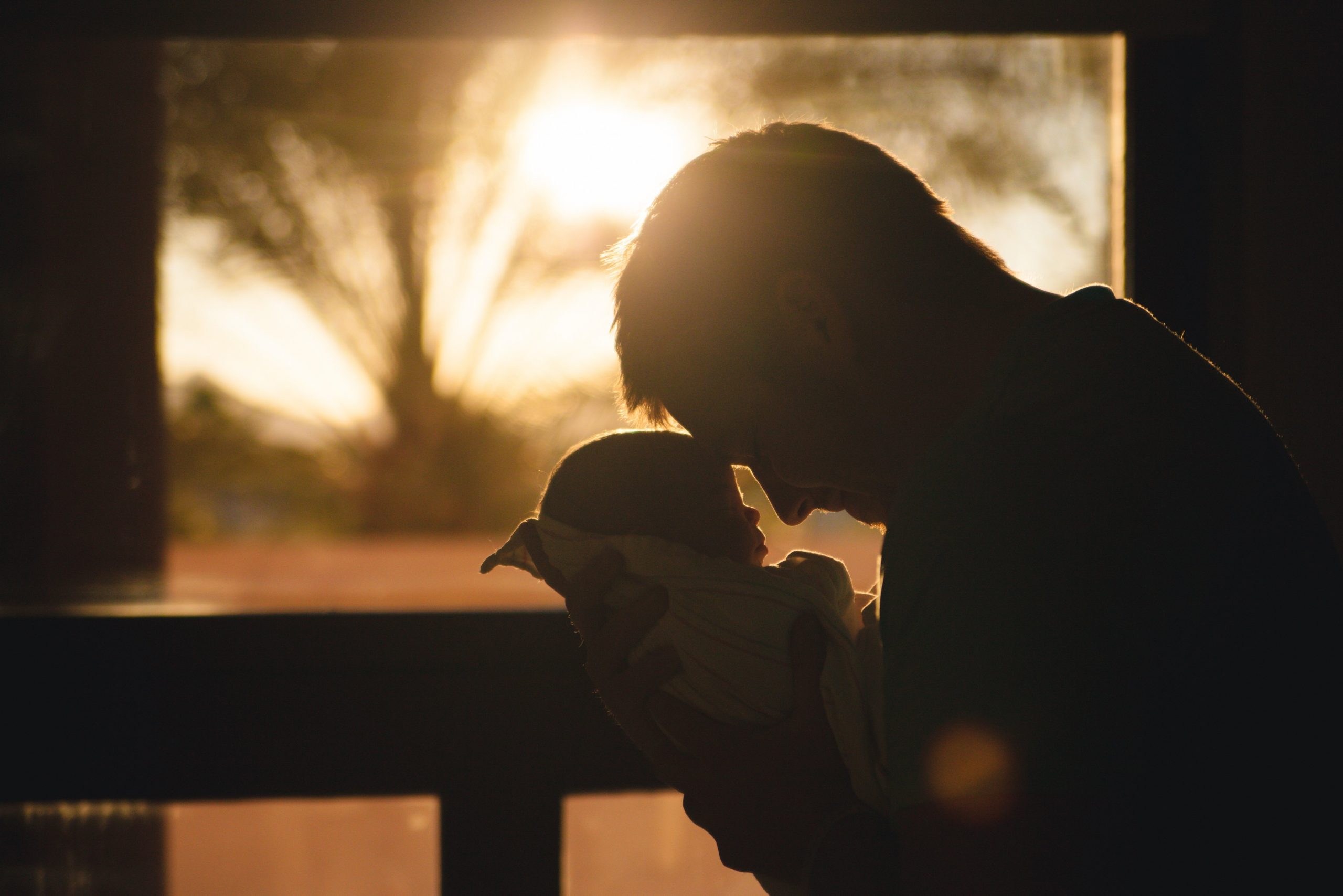 A father cuddling his Baby silhouetted against the sunrise