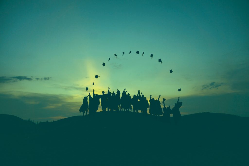 Graduates throwing their hats in the air silhouetted by the sunset.