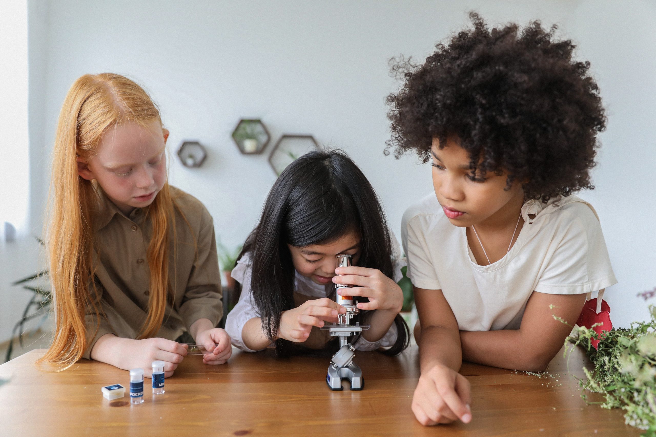 Three young children are gazing through a microscope.