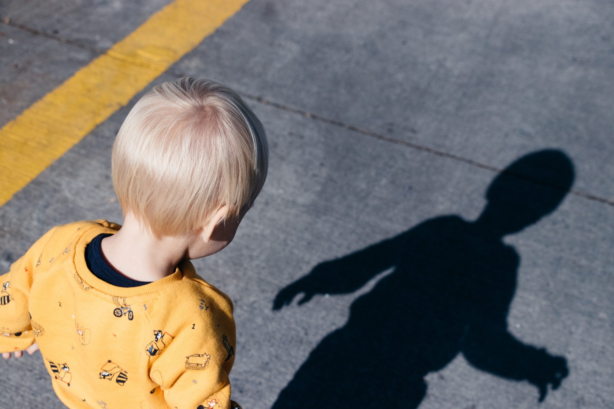 Blond Haired Toddler staring at his shadow on the pavement.