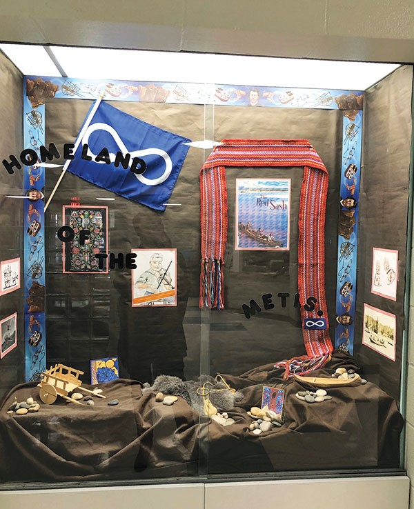 A school display case contain student artwork, a Metis Flag and Metis iconography.