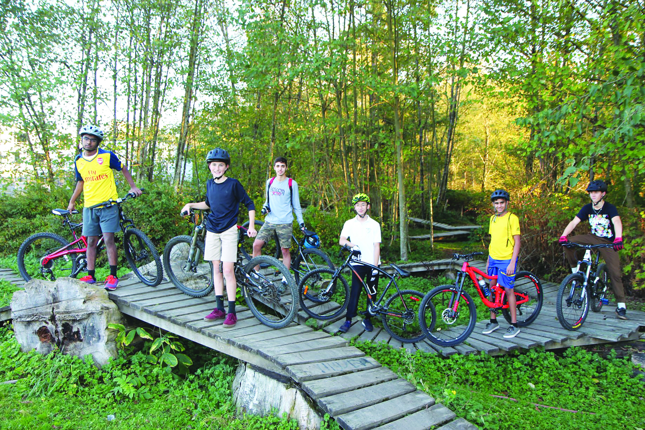 Young students stand next to their bike's on a wooden trail.
