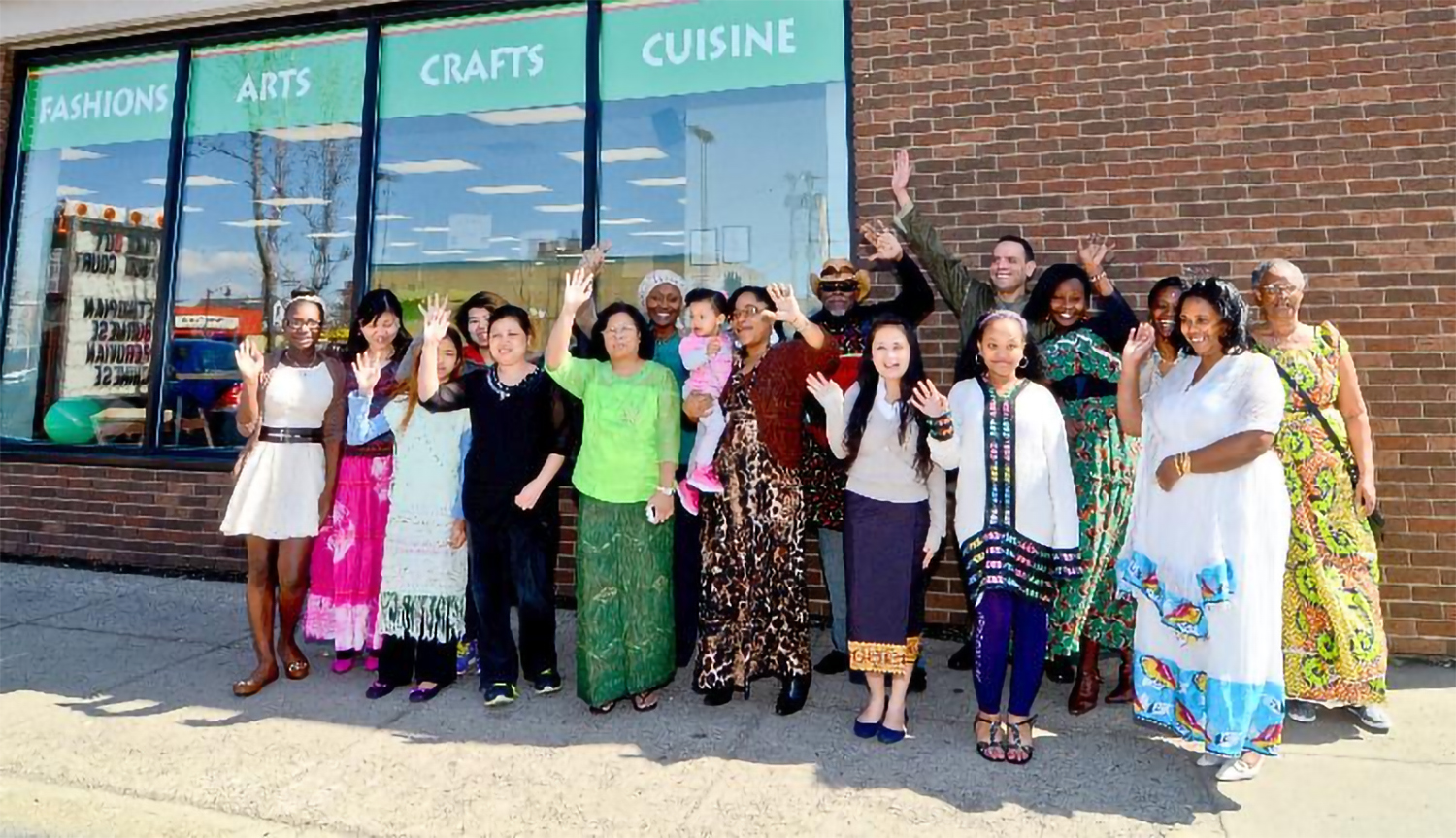 A variety of ethnic people waving in front of a store.