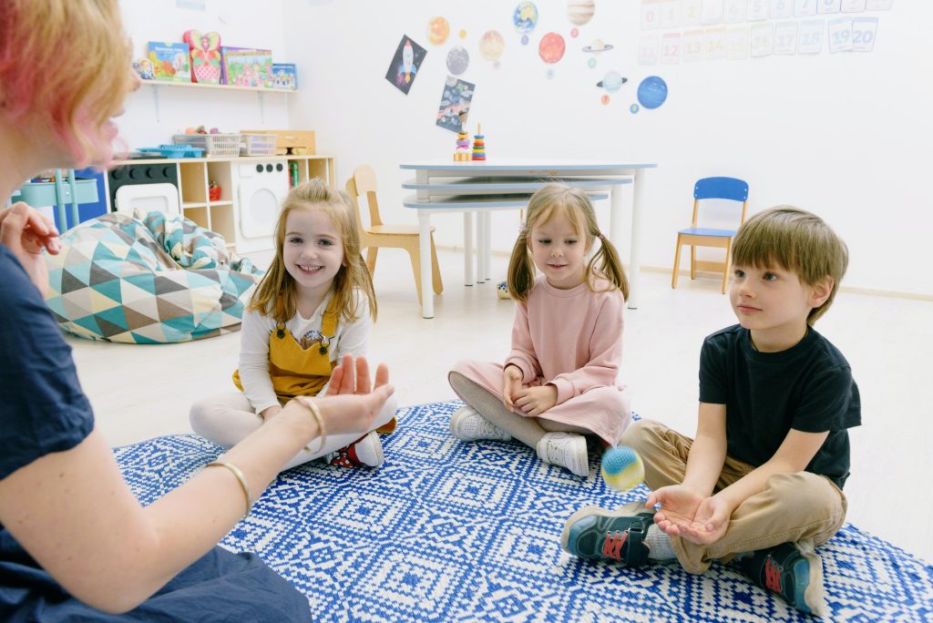 Woman speaking to three children sitting on the floor
